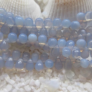 May include: A strand of light blue teardrop-shaped beads. The beads are made of chalcedony and have a translucent, iridescent finish.