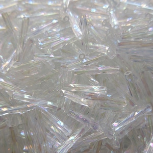 May include: A large pile of iridescent clear glass beads, shaped like long, thin cylinders.