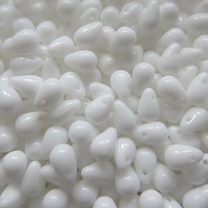 May include: A close-up image of a large quantity of white teardrop-shaped glass beads. The beads have a small hole at the top for stringing.