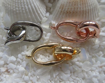 May include: Three metal clasps in silver, rose gold, and gold finishes. Each clasp is a double loop design with a smooth, rounded finish.