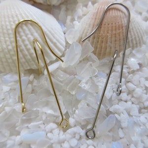 May include: Two earring hooks, one gold and one silver, are displayed on a bed of white and clear stones. The hooks are made of metal and have a simple design.