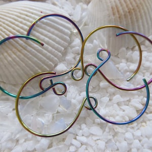 May include: Three iridescent rainbow colored metal hoops, each with a unique shape, are intertwined and displayed on a white background.