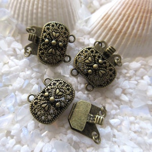 May include: Four antique gold-toned metal clasps with intricate floral designs. Each clasp has three loops for attaching jewelry.