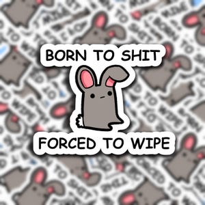 May include: A sticker featuring a cartoon bunny with pink ears and a white tail. The text "BORN TO SHIT" is above the bunny, and "FORCED TO WIPE" is below. The background shows a blurred pattern of similar bunnies and text.