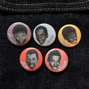 May include: Set of five round pinback buttons featuring portraits of young men. Each button has a different colored background: pink, white, yellow, red, and coral. Each button has a different name: Ronnie, Bobby, Ricky, Mike, and Ralph.