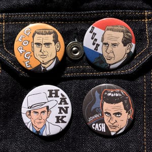 Pode incluir: Quatro botões redondos com retratos de lendas da música country. Os botões incluem imagens de George, Buck, Hank e Johnny Cash. Os botões estão colocados sobre um fundo de ganga escura.