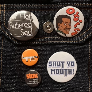 May include: A selection of circular pin badges with different designs and text. One badge says "Hot Buttered Soul," another features a portrait and the name "Otis." Other badges say "WATTSTAR 72," "SHUT YO MOUTH!" and "stax."