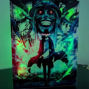 Peut inclure: Un caisson lumineux rectangulaire présentant une impression graphique vibrante d'un personnage debout devant une grande figure menaçante aux yeux rouges brillants et au large sourire édenté. L'œuvre est éclairée par des effets lumineux vert et bleu.