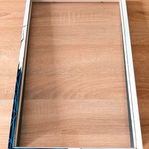 May include: Empty rectangular picture frame with a white border and a clear insert. One corner of the frame has a geometric design in blue and black. The frame is ready to be filled with a photo or artwork.