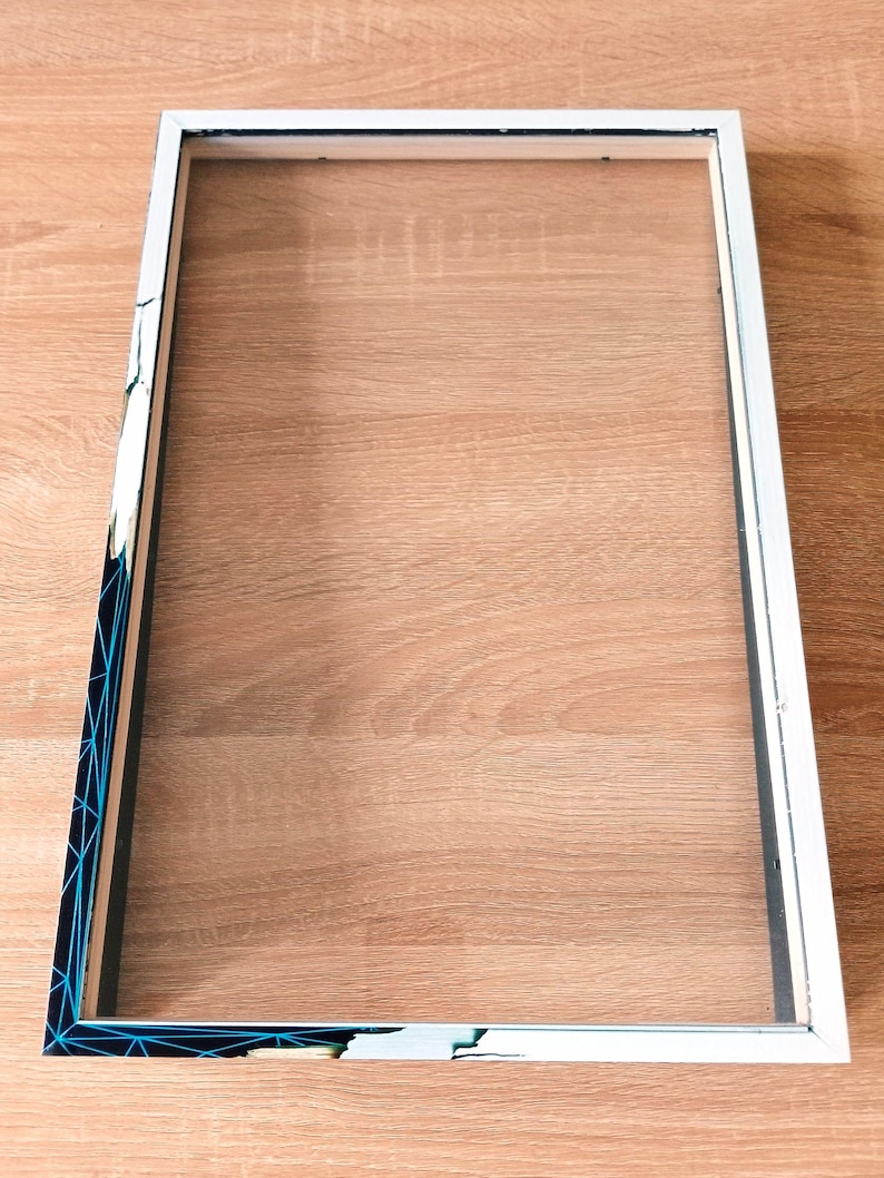 May include: Empty rectangular picture frame with a white border and a clear insert. One corner of the frame has a geometric design in blue and black. The frame is ready to be filled with a photo or artwork.