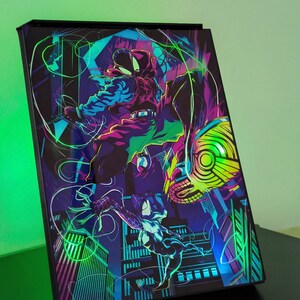 Peut inclure: Un caisson lumineux rectangulaire présentant une illustration graphique aux couleurs néon vives de deux personnages en costume de super-héros sautant à travers un paysage urbain stylisé. L'œuvre utilise des tons contrastés de violet, bleu, vert et jaune.