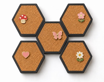 May include: Five hexagonal cork boards with black frames arranged in a cluster. The boards feature enamel pins: a red and white mushroom, a pink flower, a pink butterfly, a pink heart, and a white daisy with a yellow center and green leaves.