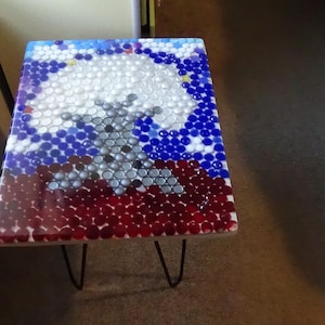 May include: A square side table with a mosaic top featuring a design of white, blue, and red elements. The table has black hairpin legs. The mosaic design appears to be made of small, round pieces.