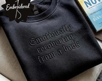 Könnte beinhalten: Ein schwarzes Sweatshirt mit Rundhalsausschnitt und einer schwarzen Ton-in-Ton-Stickerei auf der Brust, die den Schriftzug "Emotionally recovering from a book" in einer gotischen Schriftart zeigt. Das Kleidungsstück hat einen gerippten Kragen.