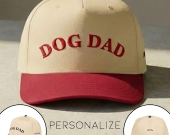 May include: A beige baseball cap with a red brim and a red button on top. The words "DOG DAD" are embroidered in red across the front. The cap has a curved brim and a structured crown, perfect for dog lovers.