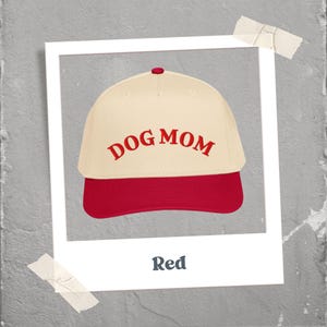 May include: A baseball cap with a cream-colored crown and a red brim. The words "DOG MOM" are embroidered in red across the front. The image is framed in a white border with the word "Red" at the bottom.
