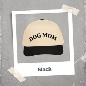 May include: A beige baseball cap with a black brim and the text "DOG MOM" in black. The cap has a black button on top. The word "Black" is written below the cap.