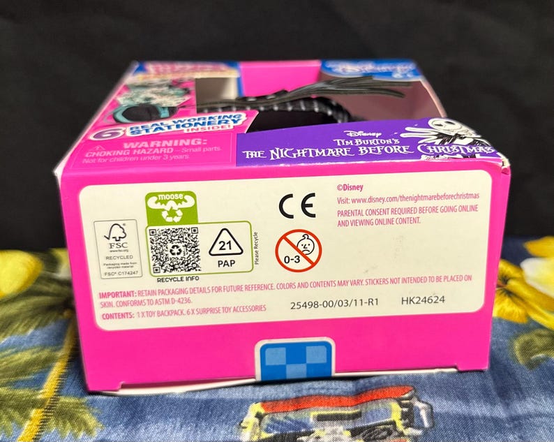 Puede incluir: Una caja rosa y azul con texto de The Nightmare Before Christmas de Tim Burton. La caja incluye advertencias, informaci&oacute;n de reciclaje y el logotipo de Disney. Contiene una mochila de juguete y accesorios sorpresa.