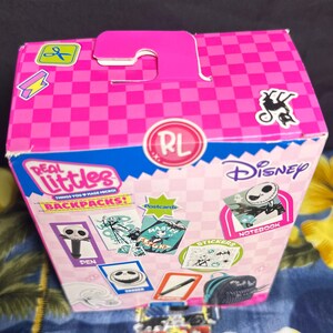 Puede incluir: Una caja rosa y azul con el personaje de Disney Jack Skellington. La caja est&aacute; decorada con pegatinas, postales y el texto "Real Littles Backpacks!".