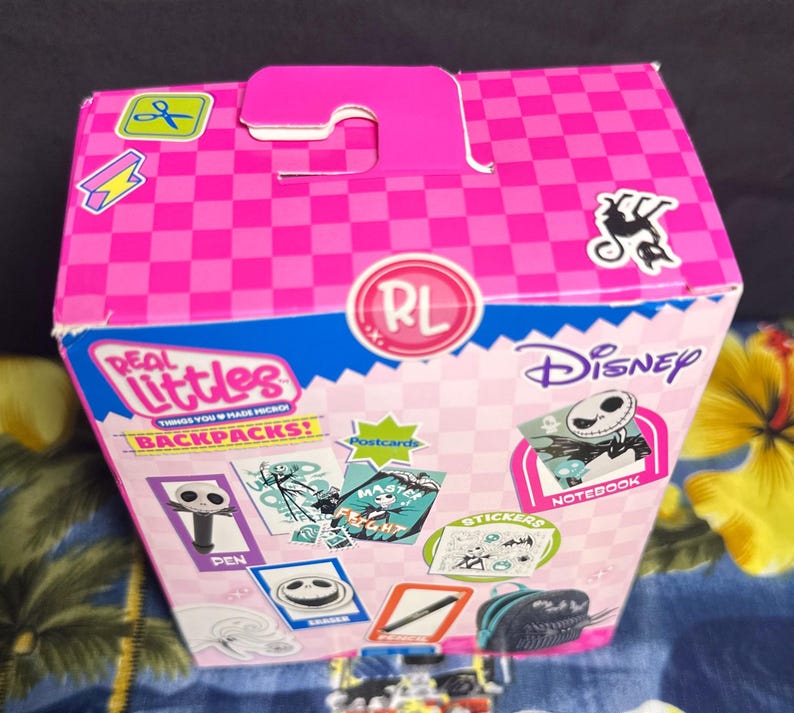 Puede incluir: Una caja rosa y azul con el personaje de Disney Jack Skellington. La caja est&aacute; decorada con pegatinas, postales y el texto "Real Littles Backpacks!".