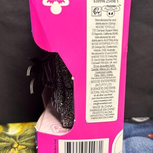 Puede incluir: Una caja de producto rosa y negra con el logotipo de Moose Toys. La caja tiene un c&oacute;digo de barras e informaci&oacute;n del producto impresa. El producto dentro de la caja es parcialmente visible.
