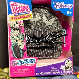 Puede incluir: Una mochila Real Littles Disney The Nightmare Before Christmas en una caja. La mochila es negra con purpurina plateada y un dise&ntilde;o de murci&eacute;lago Jack Skellington. La caja tiene el logotipo de Disney y el texto "Real Working Stationery Inside!"