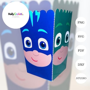 May include: A blue and green cartoon character-themed popcorn box. The box features a character's face with large eyes and a smiling mouth. The box has a scalloped top edge and is designed for a children's party or event. The HollyCraffett logo is in the upper left corner.