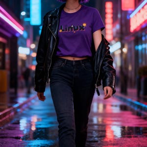 Puede incluir: Una persona lleva una camiseta morada con la palabra "Linux" y un gr&aacute;fico de sol, una chaqueta de cuero negra y vaqueros oscuros. El fondo es una calle de la ciudad iluminada con ne&oacute;n con reflejos en el pavimento mojado.