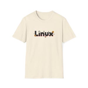 Puede incluir: Una camiseta color crema con la palabra "Linux" en una fuente estilizada. El texto es de color oscuro con peque&ntilde;os elementos decorativos, incluyendo un engranaje, una carita sonriente y una estrella. La camiseta tiene mangas cortas y cuello redondo.