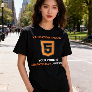 Op de afbeelding: Zwart T-shirt met de tekst "VALIDATION PASSED" boven een gestileerde oranje nummer 5, en de tekst "YOUR CODE IS SEMANTICALLY AWESOME" eronder. De persoon draagt het T-shirt op straat.