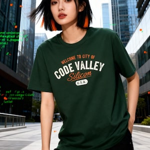 Könnte beinhalten: Ein dunkelgrünes T-Shirt mit dem Text "WELCOME TO CITY OF CODE VALLEY Silicon U.S.A." in Weiß und Orange. Das Shirt ist kurzärmlig und hat einen Rundhalsausschnitt. Der Hintergrund zeigt eine moderne Stadtlandschaft.