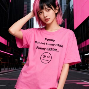 Puede incluir: Una camiseta rosa con el texto "Funny But not Funny HAHA Funny ERROR..." y un dibujo de una cara simple. La camiseta es de manga corta.