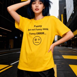 May include: A yellow t-shirt with the text "Funny But not Funny HAHA Funny ERROR..." and a surprised face graphic. The shirt is paired with black shorts. The image is taken outdoors.