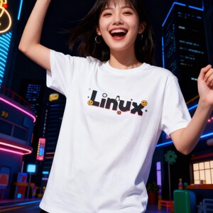 Puede incluir: Una camiseta blanca con la palabra "Linux" en una fuente estilizada, con un ping&uuml;ino y emoticonos sonrientes. La camiseta la lleva una persona sonriendo con los brazos levantados. El fondo muestra una escena urbana con luces de ne&oacute;n.