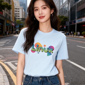 May include: A pale blue t-shirt featuring the word "Linux" in a vibrant, multi-coloured font. The t-shirt is worn with blue denim jeans. The background shows a city street scene.