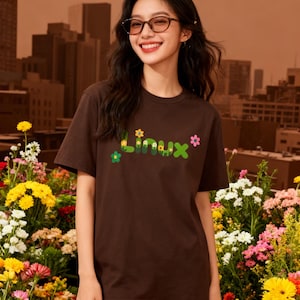 May include: A brown t-shirt with the word "Linux" in a floral design. The shirt is worn in front of a colourful flower garden. The background features a cityscape.