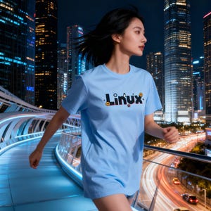 Puede incluir: Una camiseta azul claro con la palabra "Linux" en una fuente colorida y estilizada. La camiseta la lleva una persona corriendo por una pasarela moderna e iluminada por la noche, con un paisaje urbano de fondo.