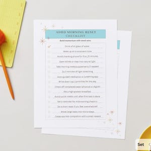 May include: A printed checklist titled "ADHD MORNING RESET CHECKLIST" with a light blue header. The checklist includes items like drinking water and avoiding social media. An orange pom-pom pen and yellow notepad are on the left.