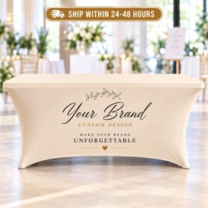 May include: A cream-colored stretch table cover featuring a black and gold printed design. The text reads Your Brand CUSTOM DESIGN MAKE YOUR BRAND UNFORGETTABLE with a small heart icon and a decorative leafy branch graphic centered on the front.