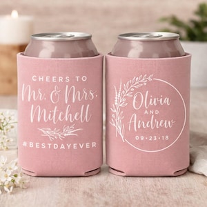 May include: Two dusty rose foam can coolers with white printed text. The left cooler reads Cheers to Mr. & Mrs. Mitchell #BESTDAYEVER. The right cooler features a circular floral wreath design with the names Olivia and Andrew and 09.23.18.
