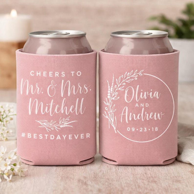 May include: Two dusty rose foam can coolers with white printed text. The left cooler reads Cheers to Mr. & Mrs. Mitchell #BESTDAYEVER. The right cooler features a circular floral wreath design with the names Olivia and Andrew and 09.23.18.