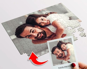 Puede incluir: Un rompecabezas rectangular con la fotografía impresa de una persona sonriente con barba que lleva a otra persona a cuestas. Una fotografía cuadrada más pequeña que muestra la misma imagen se sostiene en primer plano.