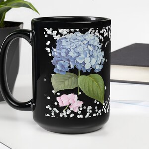 May include: Black ceramic coffee mug with a white and silver glitter background and a blue and pink hydrangea flower graphic.