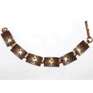Pode incluir: Um bracelete de cobre com um padrão repetido de figuras de pássaros estilizadas. O bracelete é feito de peças retangulares interligadas com uma pátina escura.