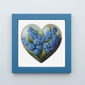 May include: A framed artwork featuring a heart-shaped design filled with blue forget-me-not flowers and green leaves. The artwork is set against a white background and framed in a blue square frame.