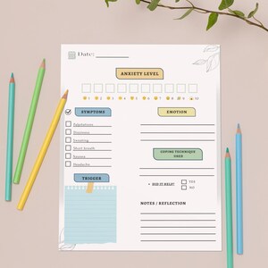 May include: A white anxiety level tracker with sections for symptoms, emotion, coping techniques, and notes. The tracker includes a scale from 1 to 10 for anxiety levels. Colored pencils in blue, green, and yellow are scattered around the tracker.