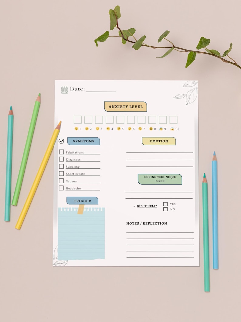 May include: A white anxiety level tracker with sections for symptoms, emotion, coping techniques, and notes. The tracker includes a scale from 1 to 10 for anxiety levels. Colored pencils in blue, green, and yellow are scattered around the tracker.