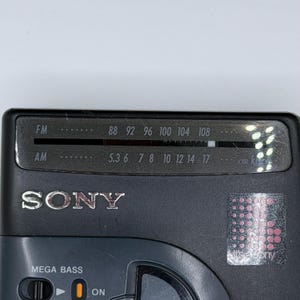 May include: A close-up of a black Sony radio. The radio has an FM and AM dial, with the FM dial showing frequencies from 88 to 108. The radio also has a "MEGA BASS" feature and an "ON" switch.