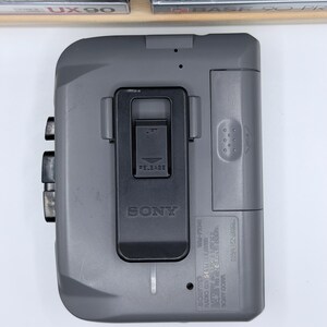 Peut inclure: Un lecteur de cassettes Walkman Sony WM-FX41 gris. Le lecteur poss&egrave;de un clip noir, des boutons et un m&eacute;canisme de lib&eacute;ration. Le logo Sony est visible. Appareil audio vintage.