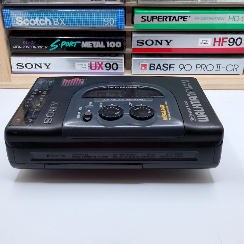 May include: A black Sony Walkman FM/AM cassette player with the text "Mega Bass" and "Walkman FM/AM" printed on the device. The player has two control knobs and a display. Cassette tapes are visible in the background.